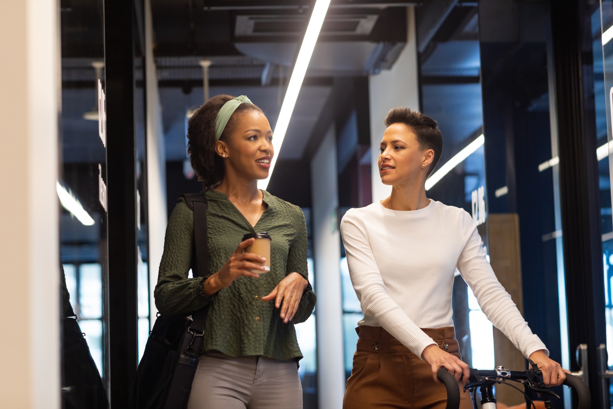 Biracial businesswoman with bicycle discussing with african american colleague in corridor of office