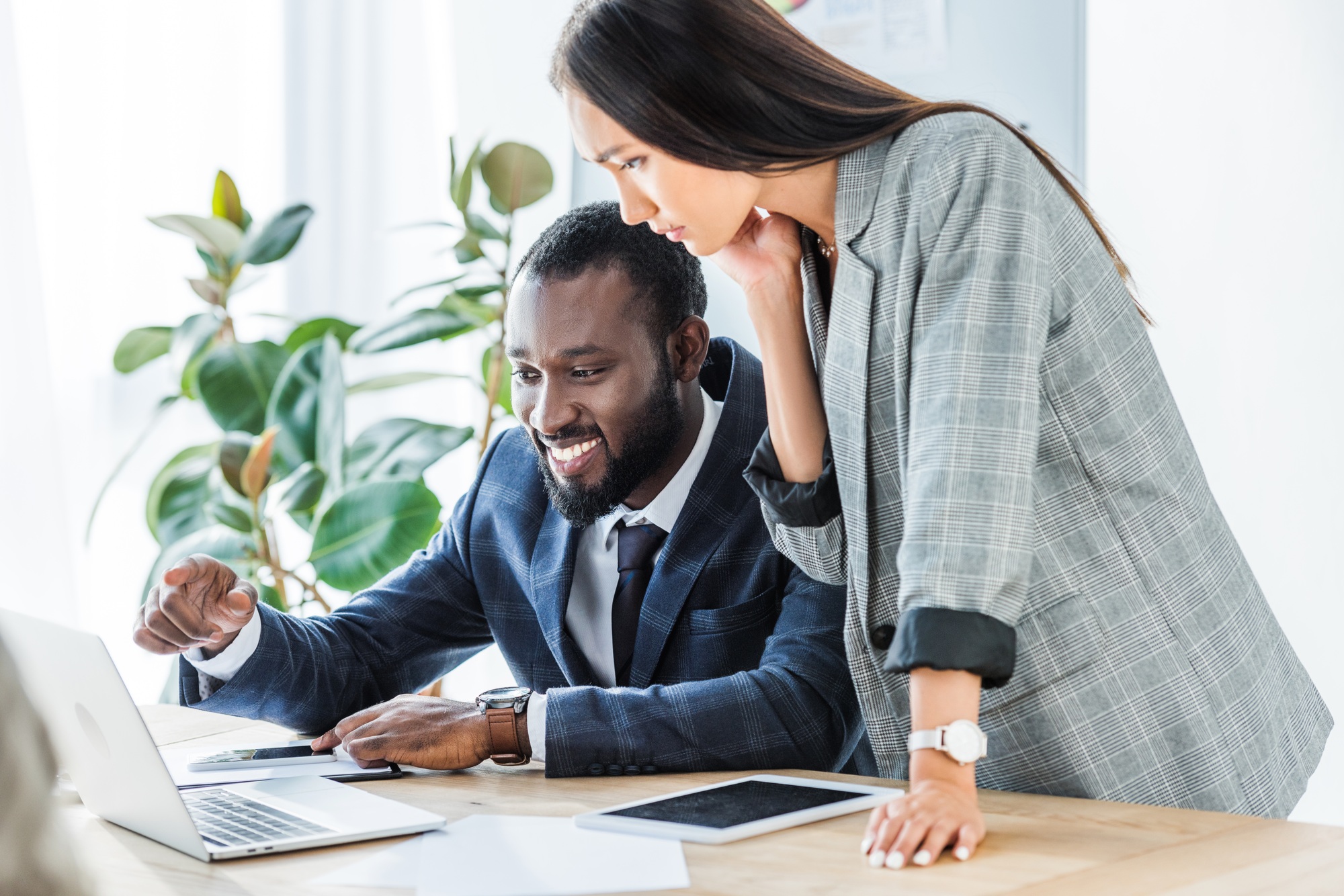 smiling african american businessman pointing on something at laptop to asian businesswoman